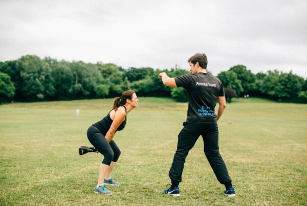 Personal trainer coaching a client performing kettlebell swings during an outdoor fitness session.