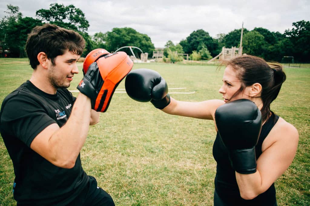 Female client doing pad work with Personal Trainer in outdoor session in Essex