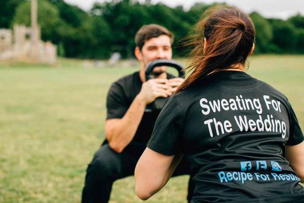 Personal trainer in Essex coaching a client through a kettlebell squat during outdoor fitness training for wedding preparation