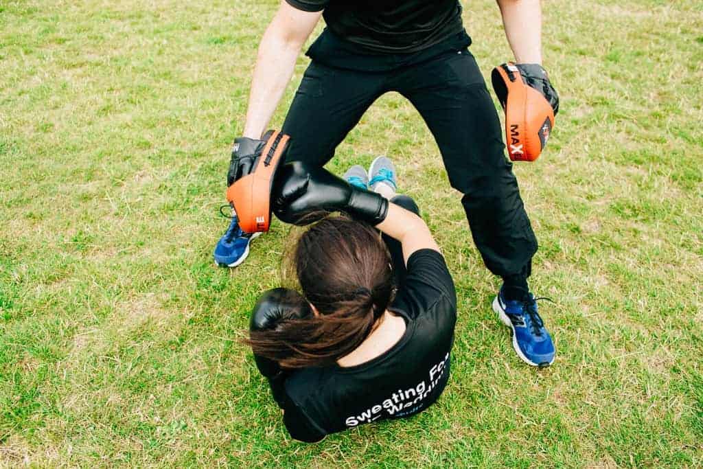 Personal training in Essex – woman performing core twists with boxing gloves and trainer holding pads outdoors